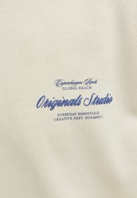 Υφασμα εκρού με μπλε κείμενο που γράφει "Copenhagen Roots Global Reach Originals Studio Everyday Essentials Creative Dept Holmen" εκτυπωμένο σε αυτό.