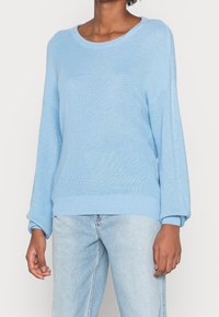 Jasnoniebieski sweter z dzianiny o okrągłym dekolcie, opadających ramionach i długich rękawach. Posiada prążkowane mankiety i dół, co dodaje mu tekstury.