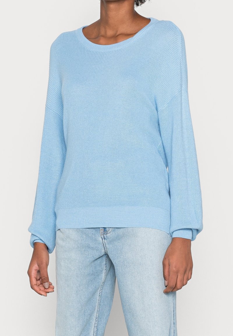 Maglione lavorato a maglia azzurro chiaro con scollo rotondo, spalle scese e maniche lunghe. Presenta polsini e bordo in costina per un'aggiunta di texture.