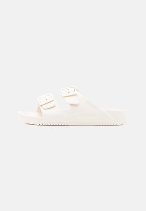 Hvide slide-sandaler med to justerbare spænder. Fremstillet af glat materiale med sål af struktureret materiale og let buestøtte.