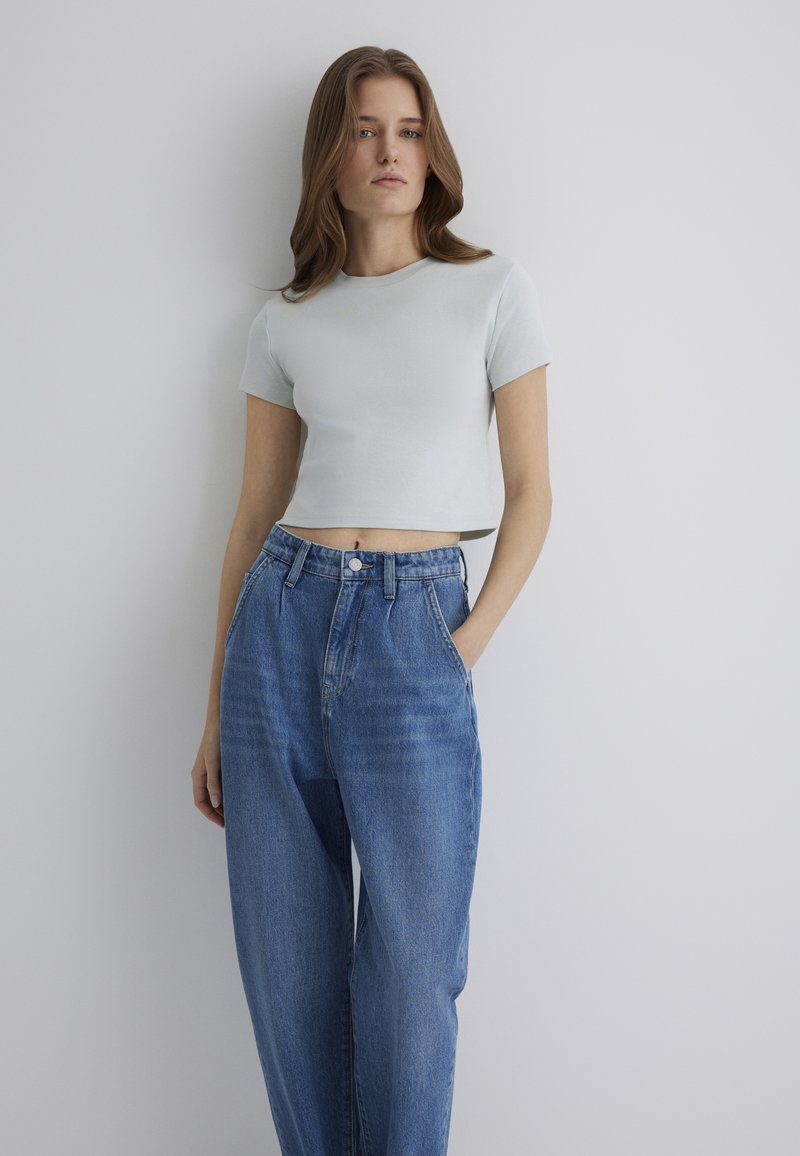 Light blue cropped t-shirt with short sleeves paired with high-waisted, loose-fitting blue denim jeans featuring front pockets and a button closure.