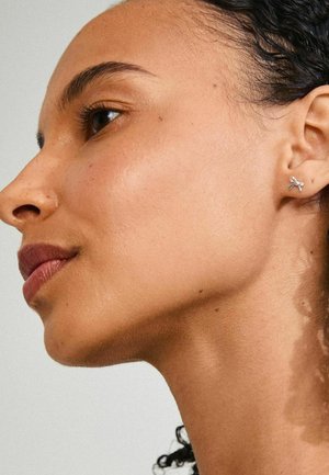 Silver stud earring in a butterfly design, featuring smooth, polished surfaces. The model has a light, natural skin tone.