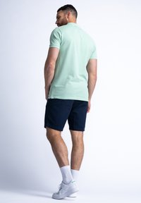 Mintgrön kortärmad polo skjorta kombinerad med marinblå shorts. Personen bär vita sneakers med gröna accenter och vita ankelsockor.