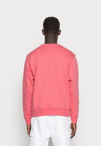 Rosa sweatshirt med rund halsringning och ribbade ärmslut. Tyget verkar mjukt, med en slät yta; bärs tillsammans med vita cargobyxor.
