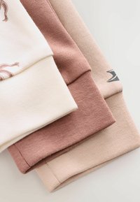 Trzy rękawy bawełnianych bluz: kremowy, przybrudzony róż i miękki beż. Żebrowana faktura, różne szerokości przy mankietach, minimalistyczny design.