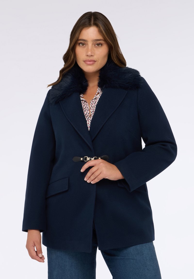 Navyblauer Mantel mit gefälschtem Pelzkragen, großen Revers und tailliertem Gürtel. Verfügt über zwei Vordertaschen und einen weichen, strukturierten Stoff.