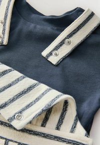 Tumedat sinine kootud särk, millel on tekstuuriga kreemja ja tumeda sinise triibulise kaeluse, varustusena nööbid ja sile kangapind.
