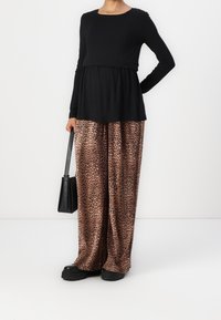 Černé dlouhé rukávy ve spojení s ležérními kalhotami širokého střihu s leopardím potiskem. Oblečení má volný střih a texturovaný design. Doplněné černou kabelkou.
