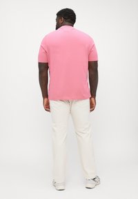 Short-sleeve, pink polo shirt with a smooth texture, paired with light beige pants. The outfit features a relaxed fit and simple design.