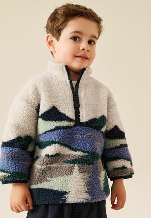 Young boy wearing a textured fleece pullover with abstract blue, green, gray, and white patterns and a black zipper collar.