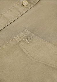 Camicia beige con bottoni caratterizzata da una tasca con ricamo di un teschio e delle ossa incrociate, realizzata in un morbido tessuto testurizzato.