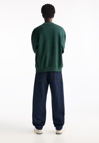 Green sweatshirt with a relaxed fit and ribbed hem, paired with loose, dark blue denim jeans. Simple design, no visible patterns.