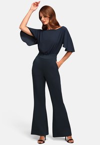 Marineblauwe jumpsuit met korte fladdermouwtjes, een getailleerde taille en wijde broekspijpen. Gemaakt van zachte stof met een vloeiend ontwerp.