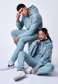 Set di felpa e pantaloni della tuta di colore blu chiaro realizzato in morbido tessuto, con un logo bianco, polsini a coste e scarpe da ginnastica bianche abbinati.