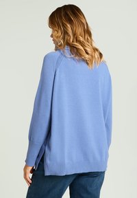 Pull en maille bleu clair à coupe décontractée, fentes latérales à l'ourlet et poignets côtelés. Le dos présente une conception d'épaule sans coutures.