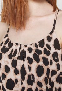 Savannah-mönstrad topp med en mjuk rosa bakgrund och stora svarta fläckar, tillverkad av lättviktsmaterial, med smala justerbara band och rynkade detaljer.