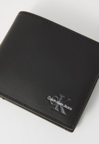Black leather wallet with smooth texture, contrasting white stitching, and embossed "Calvin Klein Jeans" logo on the front.