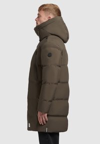 Péřová bunda ve tmavě olivově zelené barvě, s kapucí, polstrovaným designem, zipovou náprsní kapsou a logem na rukávu.