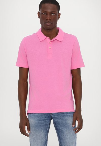 Polo shirt rose avec col, manches courtes, patte de boutonnage à trois boutons et une texture douce. Porté avec un jean bleu ajusté.