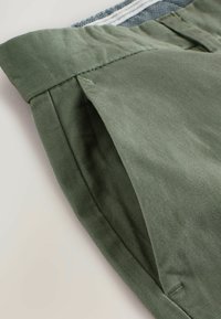 Pantalones cortos verde oliva fabricados en un tejido suave, con una cinturilla doblada y detalles cosidos. Bolsillos laterales con una ligera línea visible.