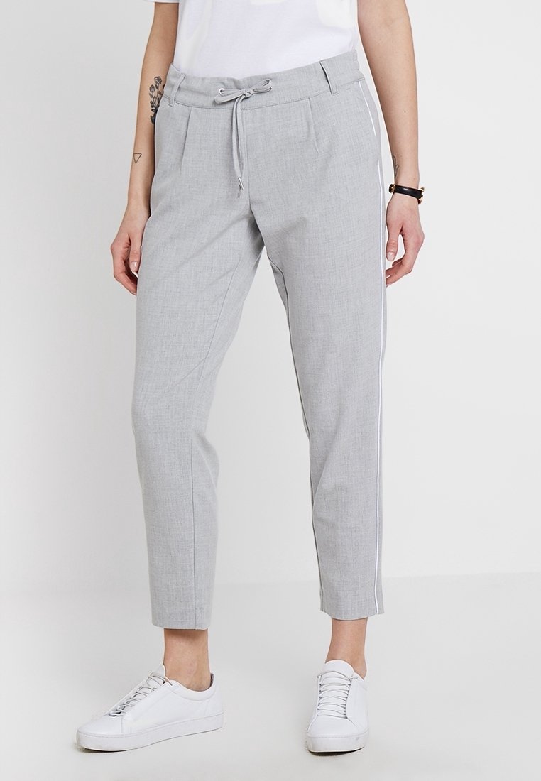 Personne portant un pantalon gris clair fuselé avec une taille à cordon de serrage et des rayures blanches sur les côtés, associé à des baskets blanches et un haut blanc.