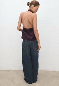 Back view of a person wearing a sleeveless, dark purple top and loose, dark blue denim jeans with a high waist. Simple design, no visible patterns.