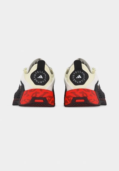 Par črno-belih športnih copat z rdečim vzorčastim petami in logotipom Stelle McCartney na zadnjih zankah za vlečenje.
