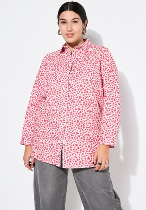 Camicia a maniche lunghe di tessuto rosa con motivo a cuori, caratterizzata da una chiusura con bottoni e una vestibilità rilassata. Pantaloni grigi con una linea larga.
