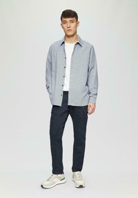 Chemise boutonnée bleu clair avec un motif à carreaux blancs, pantalon cargo bleu marine, et baskets beiges avec des accents verts. Vue de dessus.