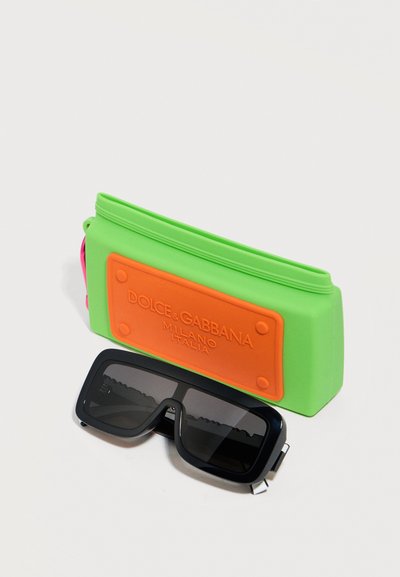 Μαύρα ορθογώνια γυαλιά ηλίου δίπλα σε μια πράσινη και πορτοκαλί θήκη με το λογότυπο Dolce & Gabbana σε λευκό φόντο.