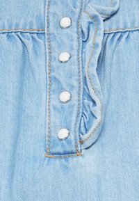 Light blue denim fabric with five shiny silver snap buttons, featuring a ruffled seam and visible stitching details.