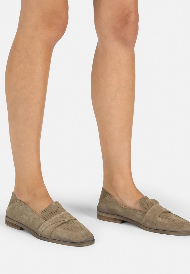 Mocasines de ante marrón claro con un panel frontal texturado y perforado, y un bajo tacón de madera, que presentan un acabado suave y acentos de diseño angulados.