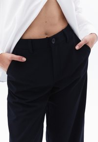 Donkerblauwe broek met een getailleerde pasvorm, voorzien van een knoopsluiting, zijzakken en een gladde stofstructuur.