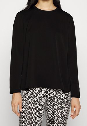 Femme portant un haut à manches longues noir uni et un pantalon noir et blanc avec un motif de texte répétitif "HUGO".