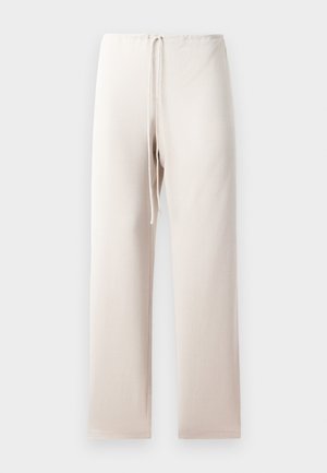 Jasno beżowe spodnie z prostym krojem, posiadające elastyczny pasek w talii oraz sznurek do regulacji. Materiał wydaje się miękki i gładki.
