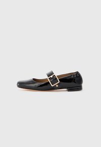 Zapato plano de charol negro estilo Mary Jane con una gran hebilla dorada y tacón bajo sobre un fondo blanco.