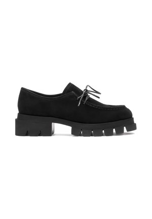 Zapatos de ante negro con cordones y suela de goma gruesa, con una superficie texturada y costuras visibles a lo largo de la parte superior.