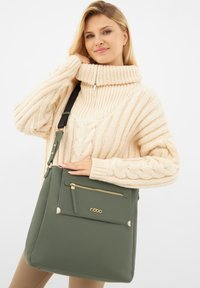 Borsa a mano in pelle verde con forma strutturata, dotata di una tasca frontale con zip e dettagli in tonalità oro. Superficie texturizzata e tracolla regolabile.