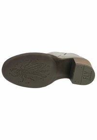 Suela de zapato de goma marrón con un diseño de insecto en relieve, con un tacón ligeramente elevado y el logotipo "FLY LONDON" en el lateral.