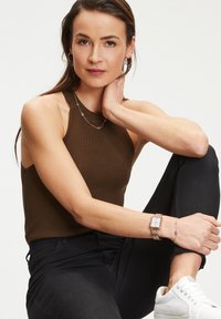 Braun gestreiftes Halstopp, schwarze Skinny-Jeans, weiße Sneakers und gestaffelter Schmuck, einschließlich einer roségoldenen Uhr und lila Akzenten.