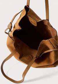 Geantă din suede bej cu accente din piele, cu deschidere de sus și margini rotunjite. Are două mânere pentru umăr și o căptușeală interioară netedă.