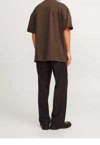 Brun bomullströja med lös passform och korta ärmar, kombinerad med svarta byxor. Enkelt mönster, inga synliga mönster eller detaljer.