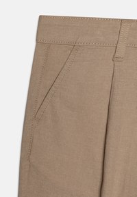 Beige bomullsbyxor med rak passform, utrustade med två sidofickor och synliga sömdetaljer längs midjan och fickorna.