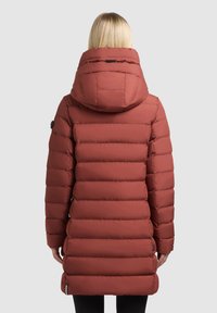 Doudoune rouge avec un col montant et une capuche, comportant des sections matelassées horizontales, des boutons noirs en décoration, et une coupe mi-cuisse.