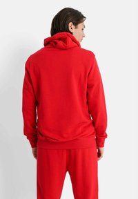 Röd hoodie gjord av mjukt tyg, med en stor huva, ribbade muddars och en avslappnad passform, i kombination med matchande röda byxor.