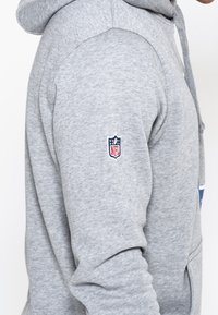 Grauer Hoodie aus Baumwollmix, mit einer Vorderentasche, Kapuze mit Kordelzug und NFL-Logo, das auf dem linken Ärmel gestickt ist.