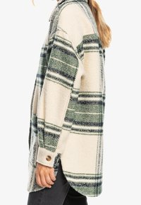 Camisa de franela de cuadros en crema y verde, con un corte holgado, puños con botones y una textura suave, con rayas más anchas en colores alternos.