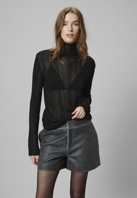 Schwarzer, gerippter Langarm-Turtleneck mit transparenter Textur und körperbetontem Design, kombiniert mit grauen Shorts aus Kunstleder, Vorderansicht.
