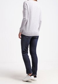 Suéter ligero gris de manga larga, combinado con jeans azul oscuro. Se llevan zapatillas blancas, mostrando un atuendo informal.