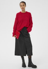 Punane kootud kampsun, must nahast seelik lõhikuga, mustad massiivsed pahkluukingad ja punane litritega õlakott. Tekstureeritud kangas ja kontrastsed värvid.